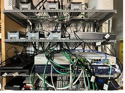 The computer rack: wire shelves carrying small servers, a network switch and a bundle of green patch cables.