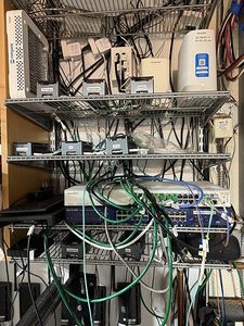 Four wire shelves of servers, switches, uninterruptible supplies and green patch cables.