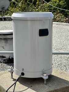 A HyQuest Solutions TB3 tipping-bucket rain gauge: a gray cylinder on three feet, on the roof.