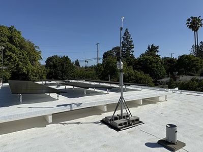 The station mast on the white foam roof beside the solar array, palms and power lines behind.