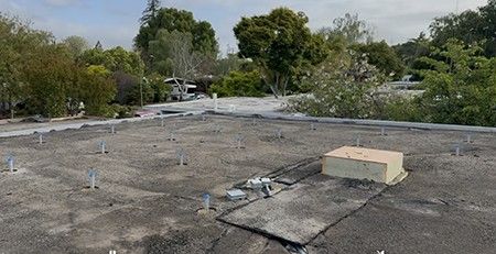 The stripped roof deck with solar mounting feet in place and a bare parapet, ready for foam.