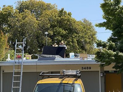 An installer’s ladder against the eave and a truck at the curb, panels going onto the roof above.