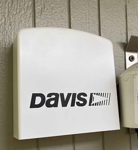 A Davis AirLink air quality sensor, a white wedge-shaped housing, mounted on a wall under an eave.