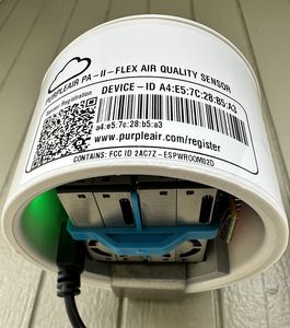 The underside of a PurpleAir PA-II-Flex sensor, showing its label, device ID and the inlet to the laser particle counter.